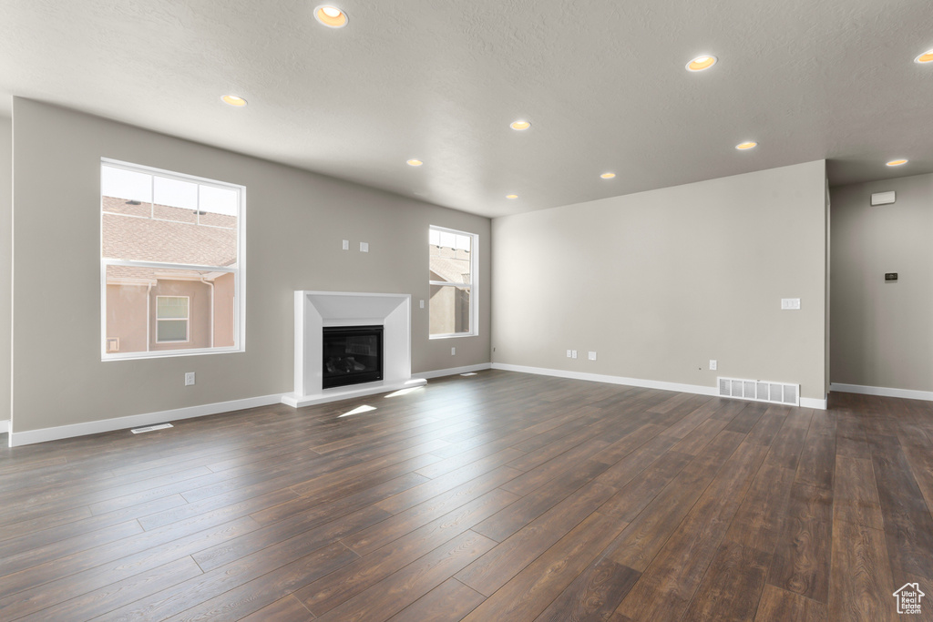 Unfurnished living room with recessed lighting, a glass covered fireplace, baseboards, and dark wood finished floors