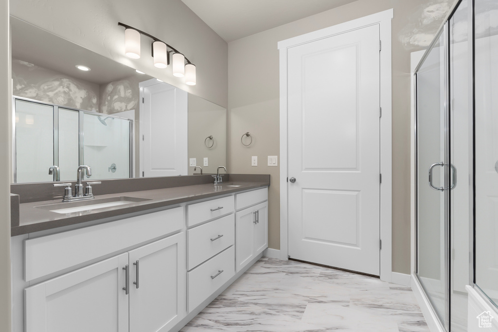 Full bathroom featuring marble finish flooring, double vanity, a shower stall, and baseboards