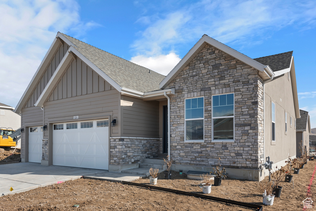 Craftsman inspired home with stone siding, board and batten siding, a garage, and driveway