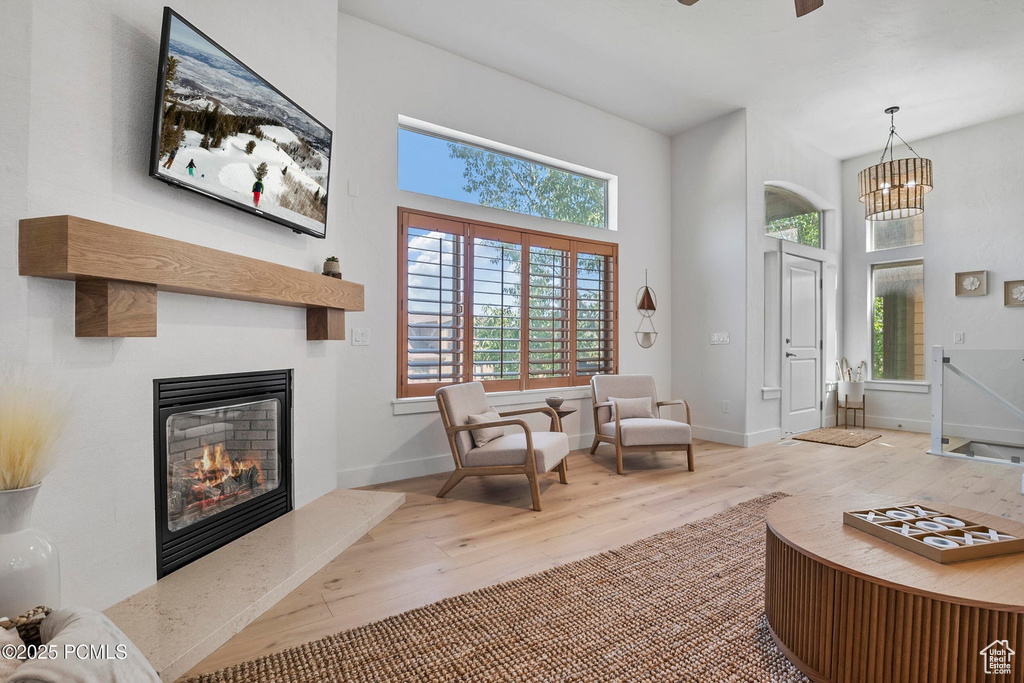 Living area with wood finished floors, a glass covered fireplace, baseboards, a high ceiling, and a chandelier