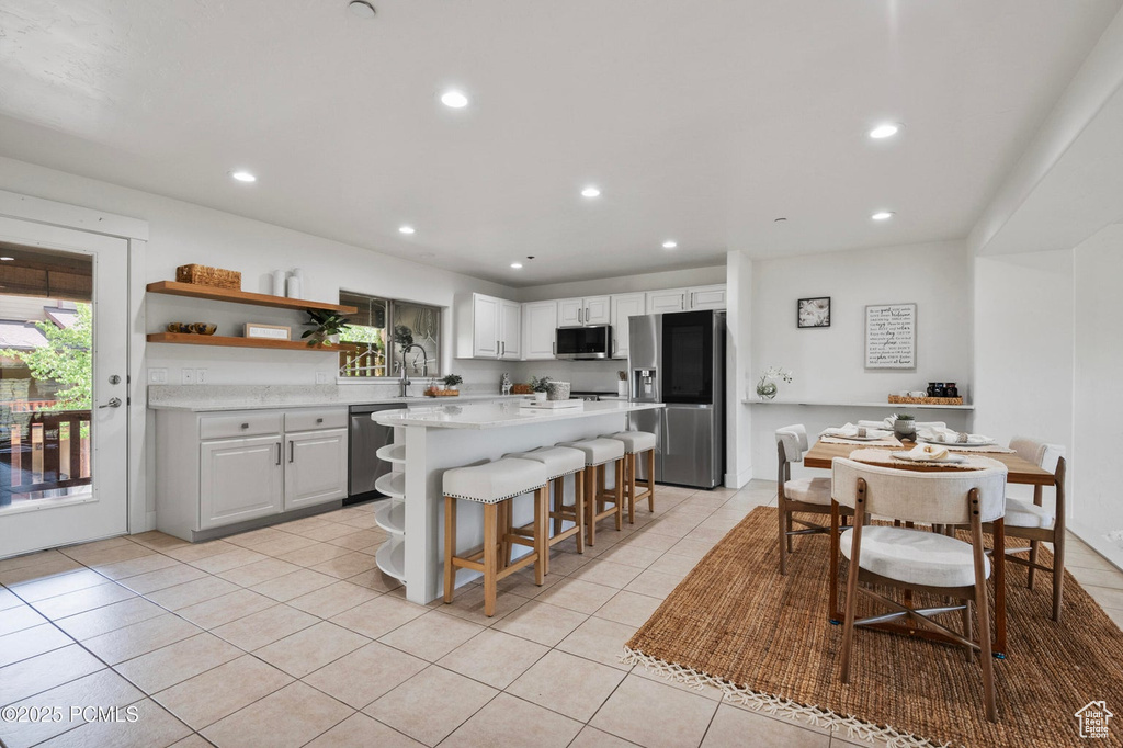 Kitchen featuring stainless steel appliances, light countertops, light tile patterned floors, a breakfast bar, and open shelves