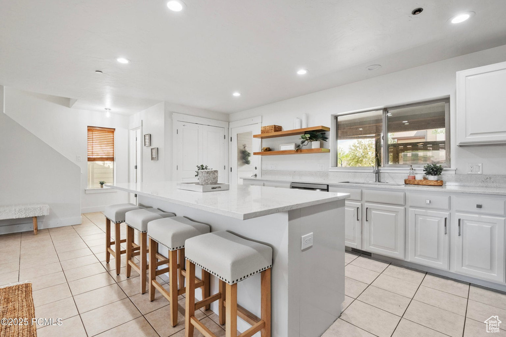 Kitchen featuring a kitchen island, light tile patterned flooring, white cabinetry, a kitchen breakfast bar, and open shelves
