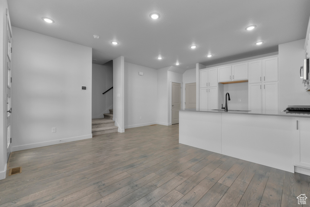Kitchen featuring wood finished floors, white cabinetry, baseboards, recessed lighting, and a sink