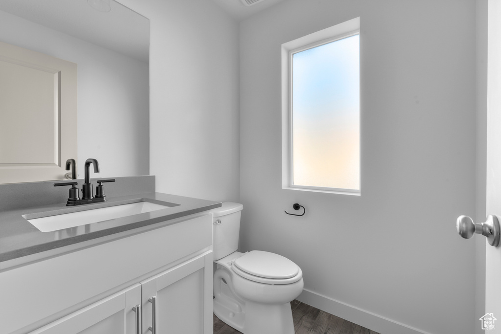 Half bath with vanity, toilet, wood finished floors, and baseboards