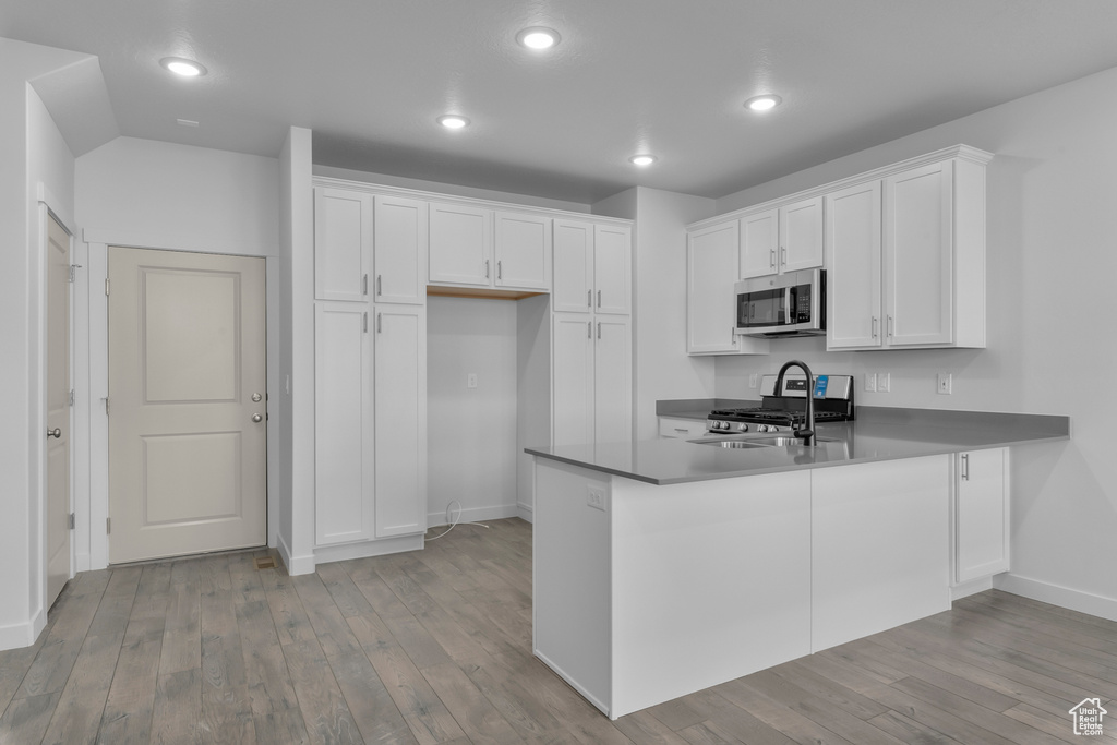 Kitchen with stainless steel appliances, baseboards, a peninsula, light wood-type flooring, and recessed lighting