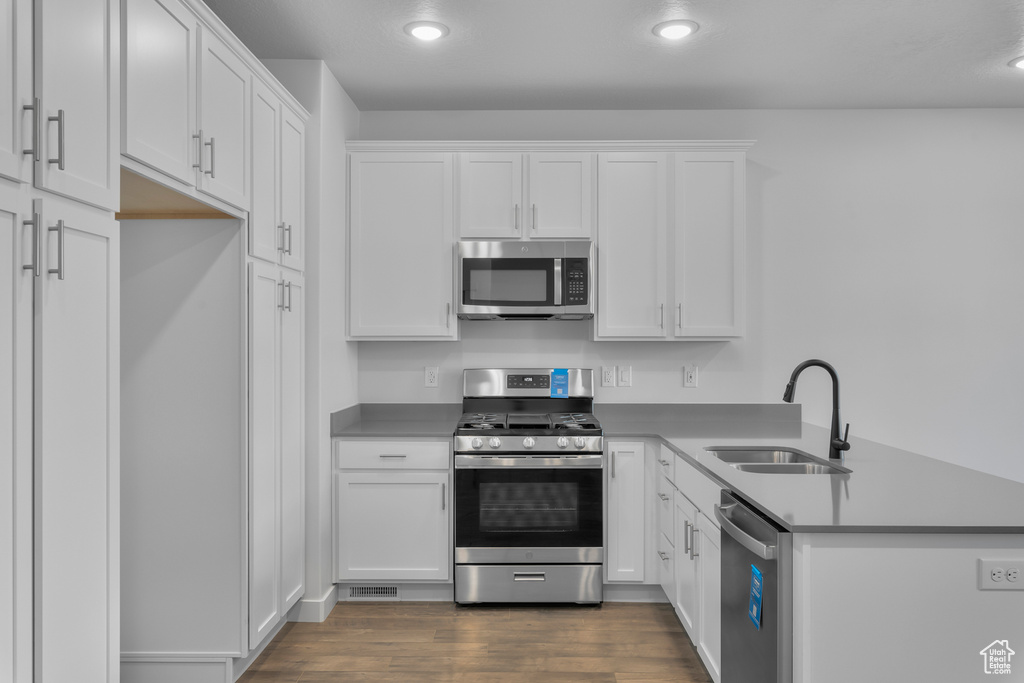 Kitchen featuring stainless steel appliances, a sink, a peninsula, white cabinetry, and recessed lighting