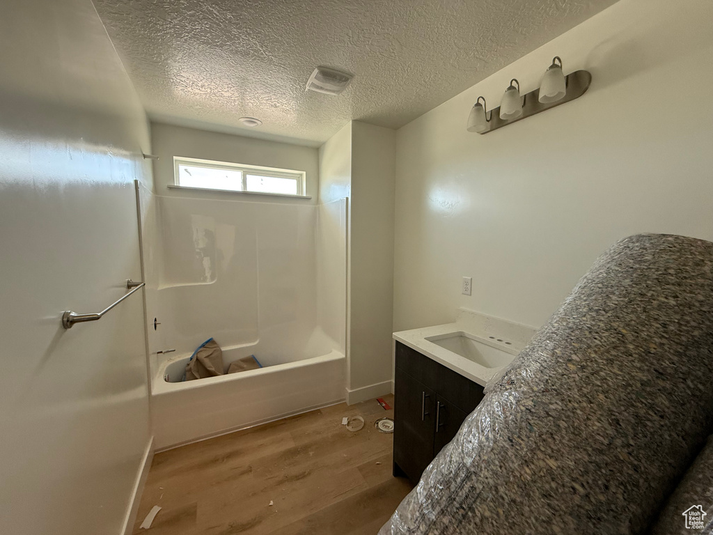 Full bathroom with wood finished floors, shower / bath combination, vanity, a textured ceiling, and baseboards