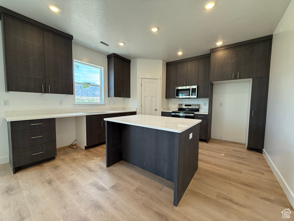 Kitchen with appliances with stainless steel finishes, light countertops, light wood-type flooring, a center island, and baseboards