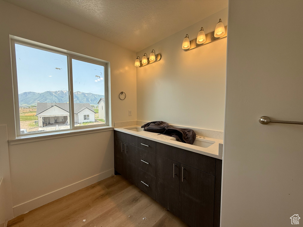 Bathroom featuring wood finished floors, baseboards, double vanity, a mountain view, and a textured ceiling