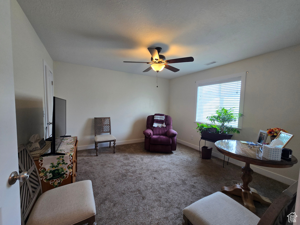 Carpeted living area featuring ceiling fan and baseboards