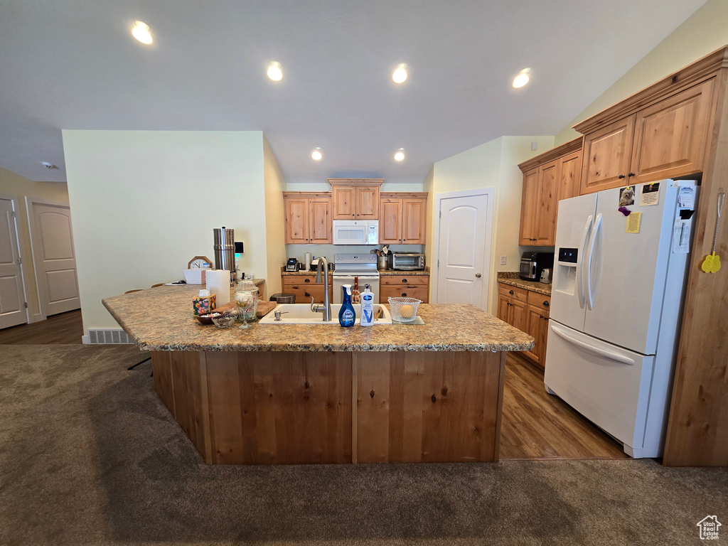 Kitchen with white appliances, a sink, a center island with sink, dark wood-style flooring, and recessed lighting