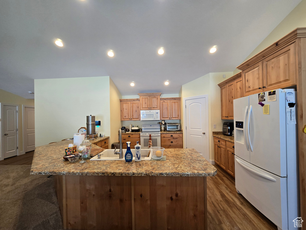 Kitchen featuring white appliances, dark wood-type flooring, a large island with sink, a sink, and recessed lighting