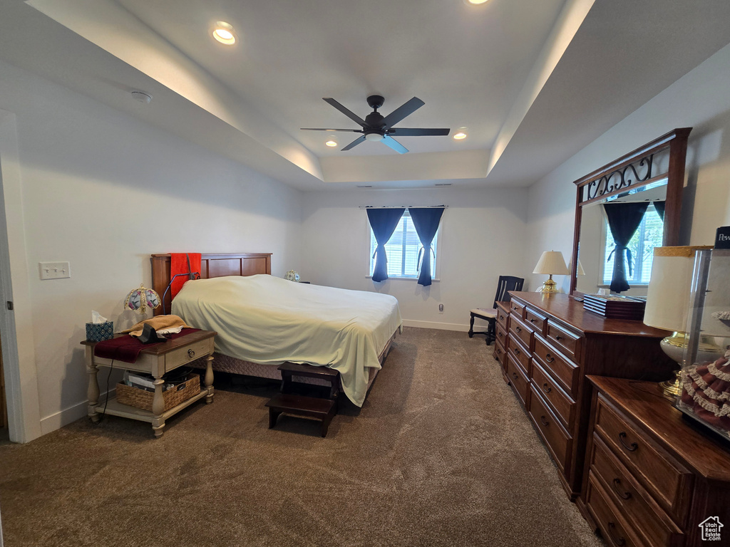 Bedroom featuring baseboards, a tray ceiling, dark colored carpet, recessed lighting, and ceiling fan