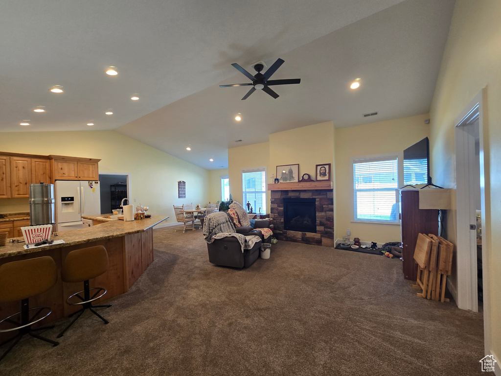 Living area with lofted ceiling, dark carpet, plenty of natural light, a ceiling fan, and a stone fireplace