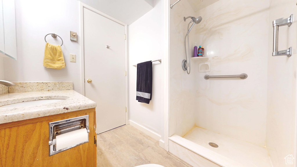 Full bathroom featuring vanity, a shower, wood finished floors, and baseboards