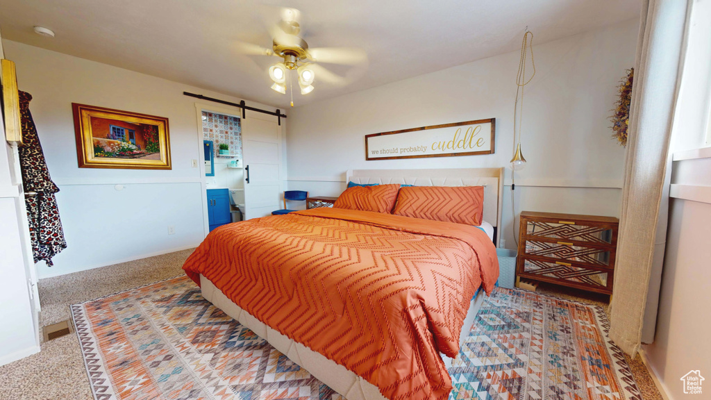 Bedroom with a barn door, carpet flooring, baseboards, and ceiling fan