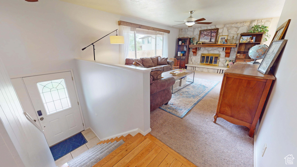 Living area with ceiling fan, wood-type flooring, and a stone fireplace