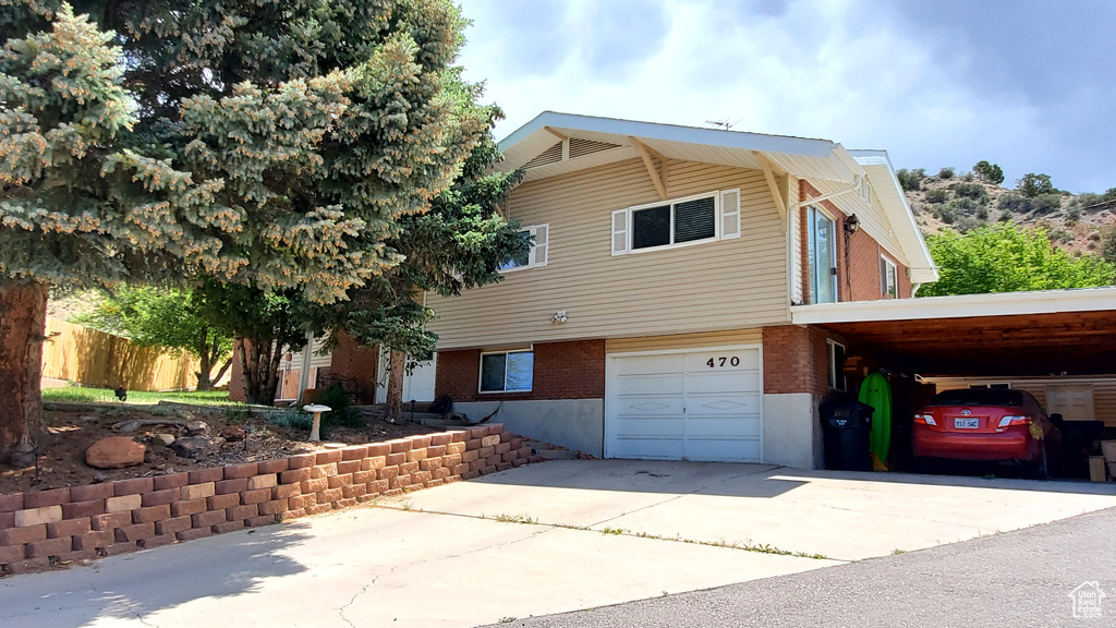 View of front of property featuring driveway, an attached garage, brick siding, and an attached carport