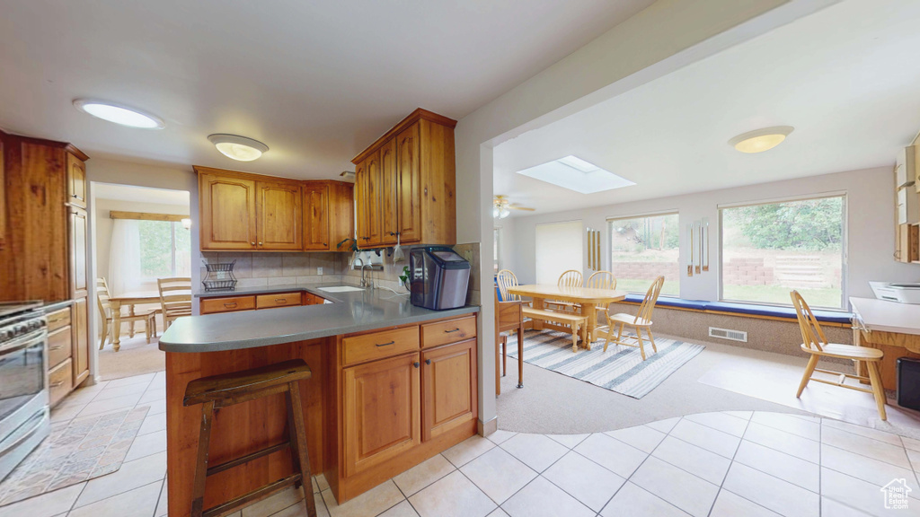Kitchen with a skylight, light colored carpet, a sink, a peninsula, and brown cabinetry