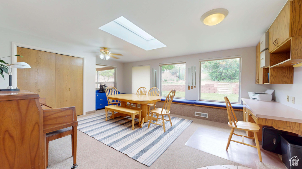 Dining space featuring light colored carpet, a skylight, healthy amount of natural light, and an office area