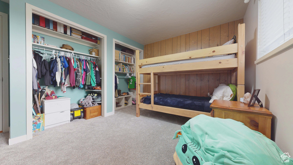 Bedroom with carpet floors, a closet, wood walls, and a textured ceiling