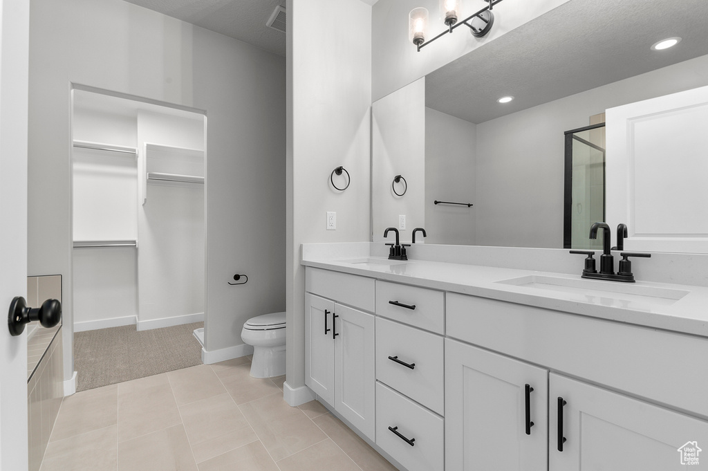Bathroom with double vanity, a shower stall, toilet, a spacious closet, and baseboards