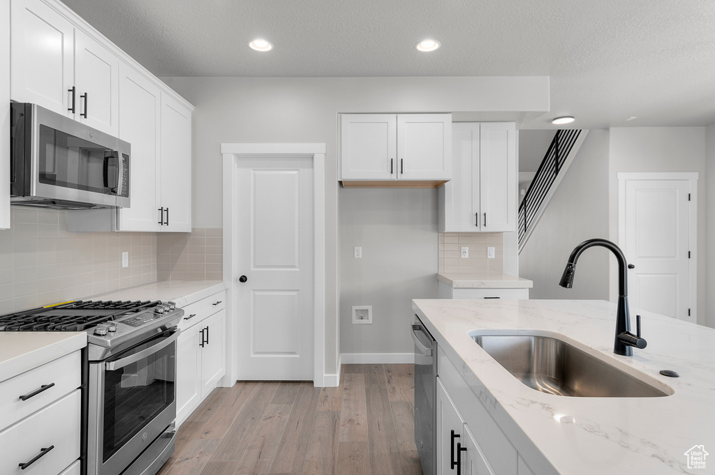 Kitchen featuring stainless steel appliances, a sink, light wood finished floors, tasteful backsplash, and white cabinets