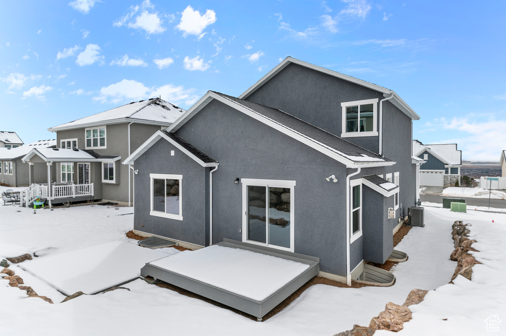 Snow covered back of property featuring central AC unit, stucco siding, and a deck