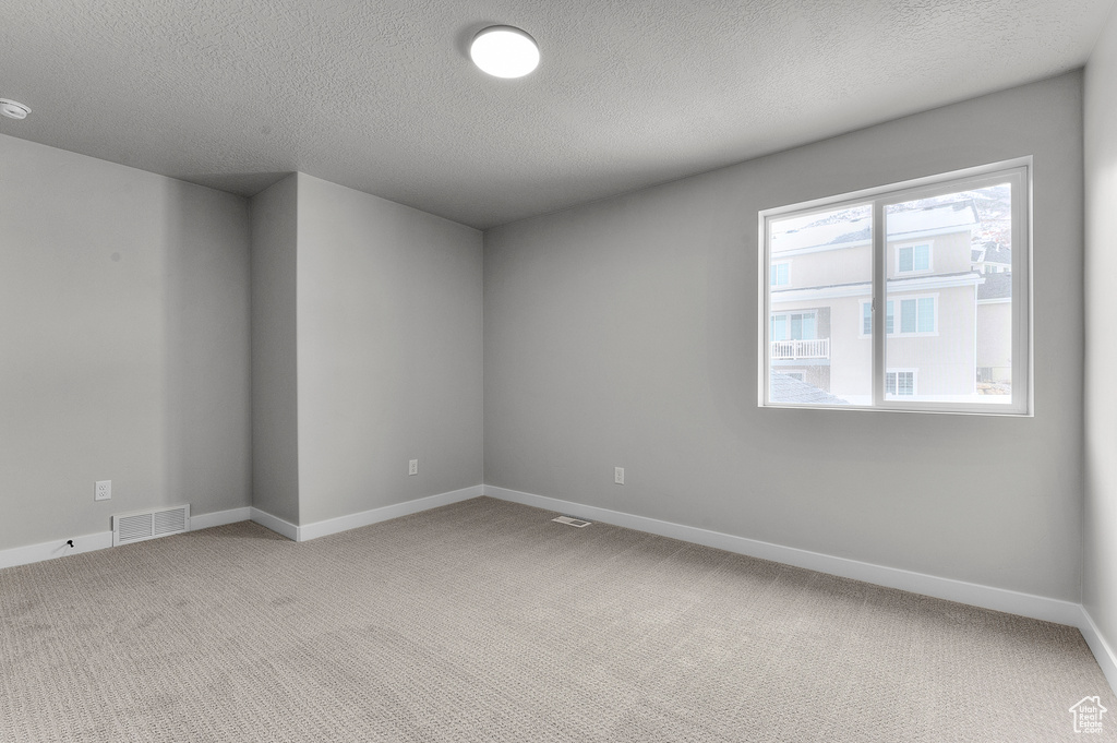 Unfurnished room featuring light carpet, baseboards, and a textured ceiling