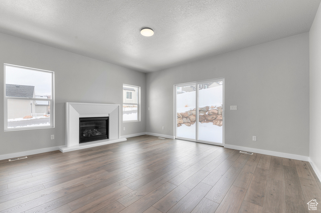 Unfurnished living room featuring baseboards, a glass covered fireplace, dark wood-style flooring, and a textured ceiling