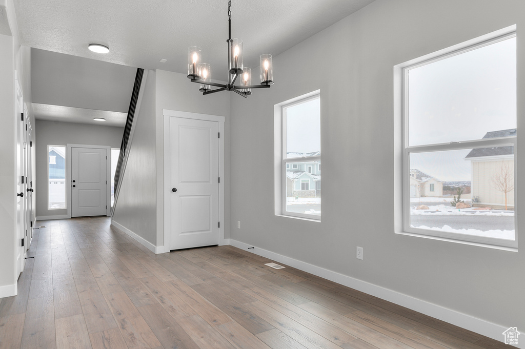 Unfurnished dining area featuring a chandelier, healthy amount of natural light, baseboards, and hardwood / wood-style flooring