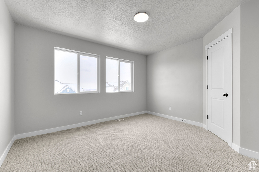 Spare room with light carpet, a textured ceiling, and baseboards