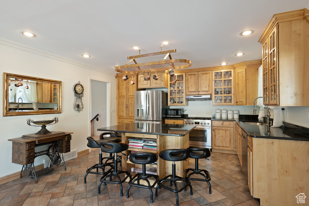 Kitchen featuring stainless steel appliances, a sink, dark countertops, ornamental molding, and stone tile flooring