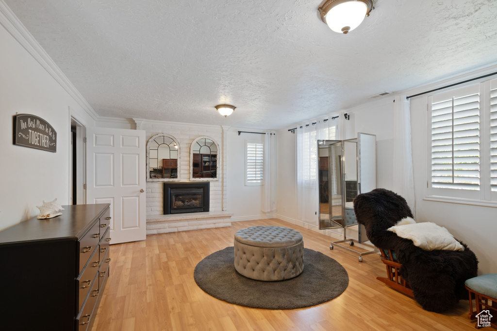 Living room featuring a fireplace, a textured ceiling, light wood-type flooring, and ornamental molding