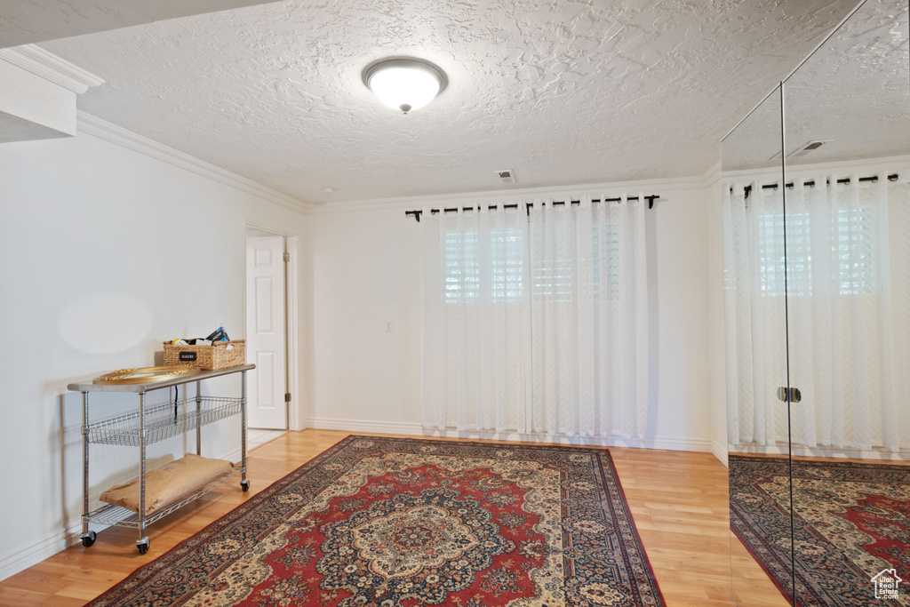 Unfurnished room featuring light wood-type flooring, a textured ceiling, healthy amount of natural light, baseboards, and ornamental molding