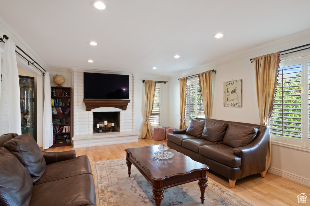 Living area with light wood-style flooring, crown molding, plenty of natural light, recessed lighting, and a fireplace