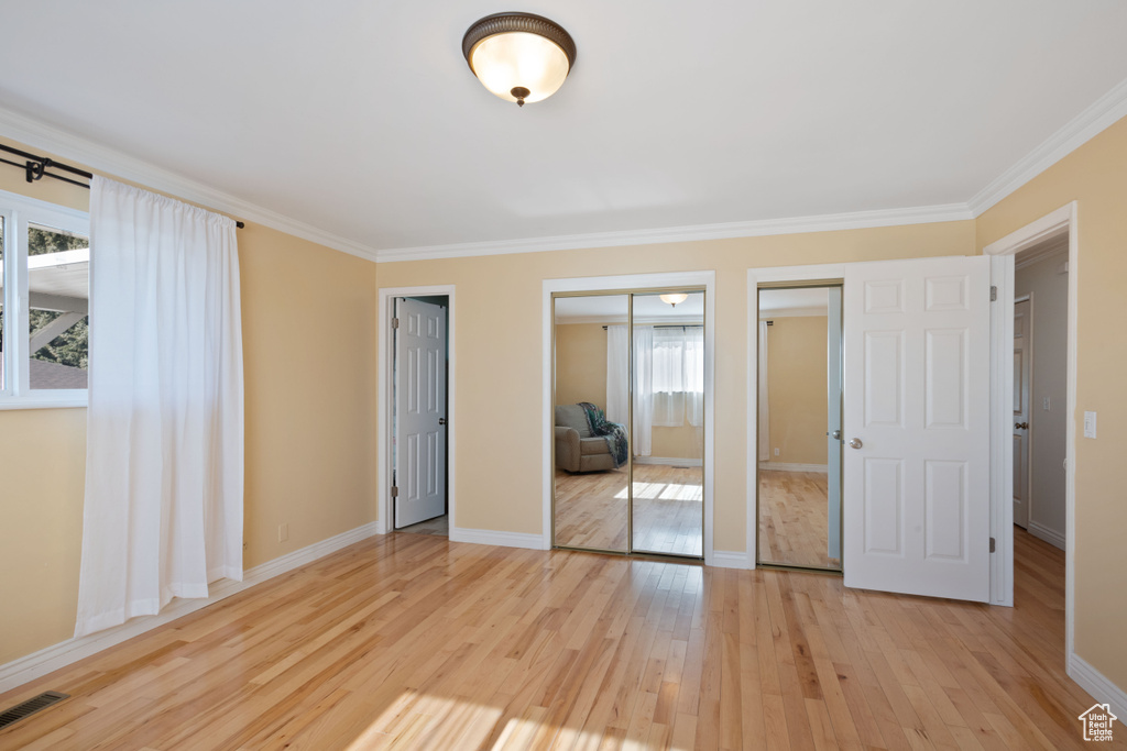 Unfurnished bedroom featuring multiple closets, light wood-type flooring, ornamental molding, and baseboards