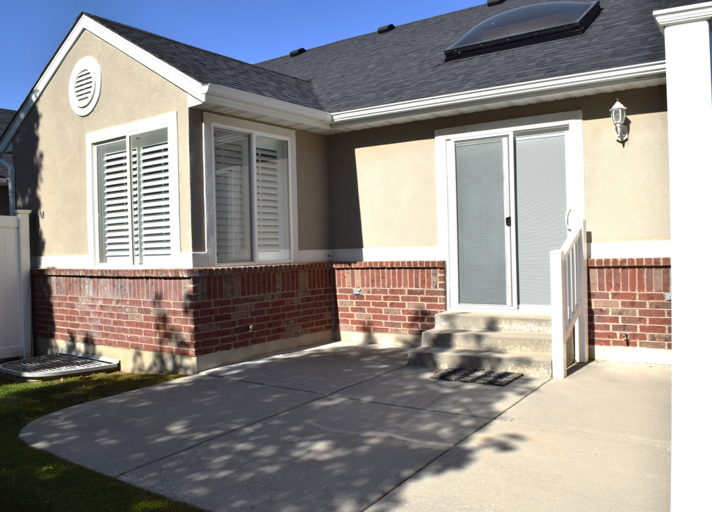 Property entrance with brick siding, a shingled roof, a patio, and stucco siding