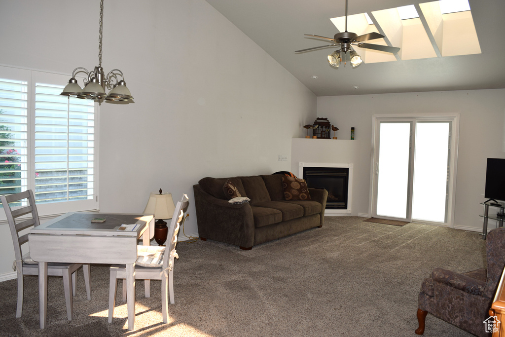 Dining space featuring a chandelier, a glass covered fireplace, carpet, a ceiling fan, and high vaulted ceiling