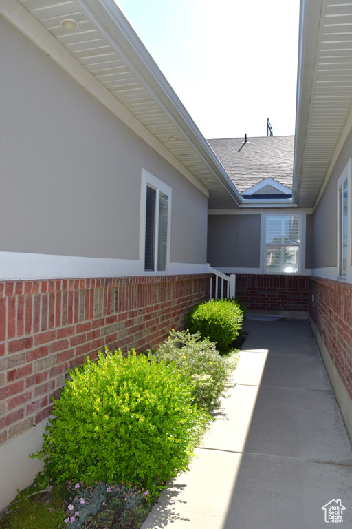 View of exterior entry with brick siding and a shingled roof