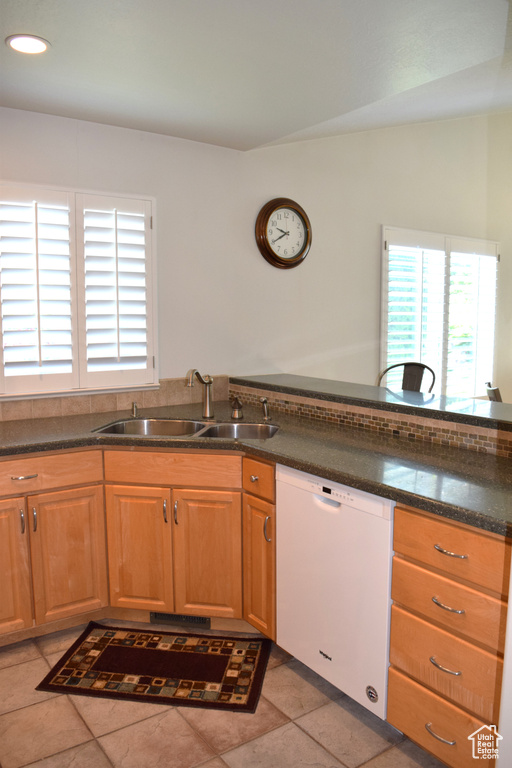 Kitchen with white dishwasher, a sink, light tile patterned floors, dark stone countertops, and recessed lighting