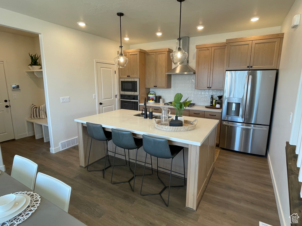 Kitchen featuring stainless steel appliances, wall chimney exhaust hood, decorative backsplash, baseboards, and a center island with sink
