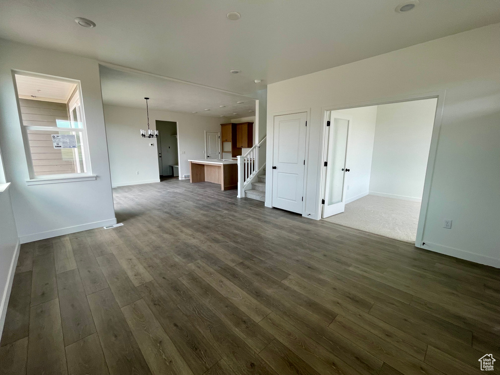 Unfurnished living room with a chandelier, dark wood-style floors, and stairs