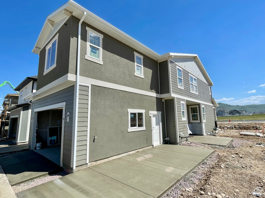 Rear view of property with an attached garage, a patio area, stucco siding, and a mountain view