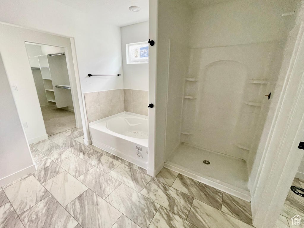 Full bathroom featuring a bath, a walk in closet, marble look tiles, and a shower