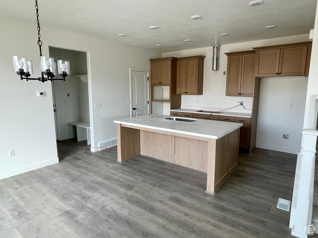 Kitchen with a chandelier, a center island with sink, wood finished floors, light countertops, and recessed lighting