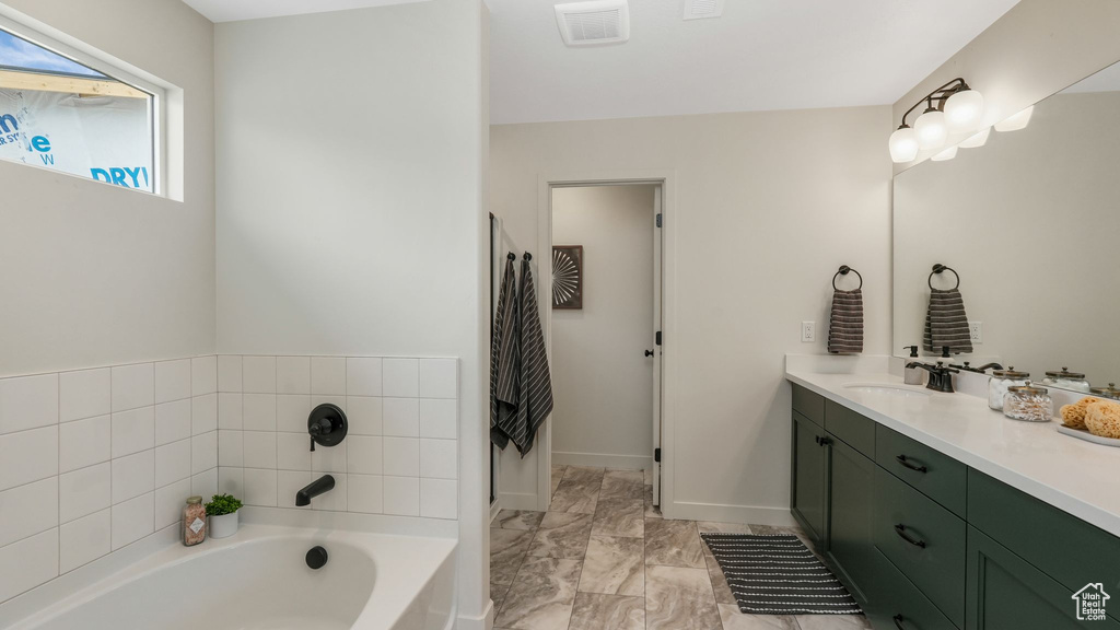 Full bath with vanity, a bath, and marble look tiles