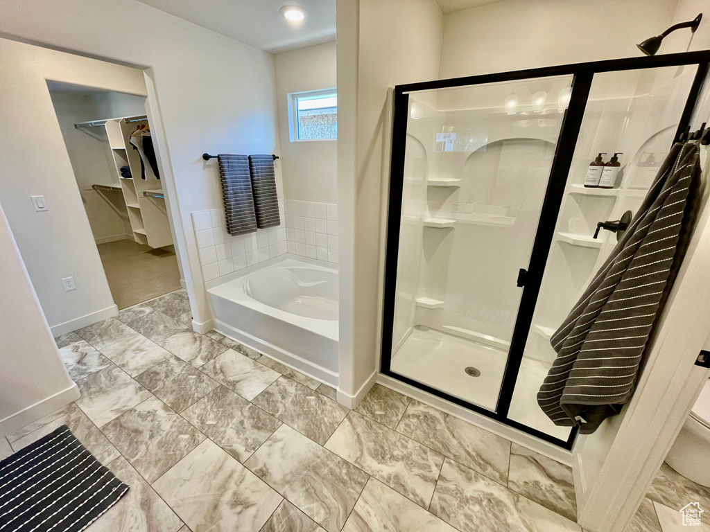 Full bathroom featuring a bath, a stall shower, baseboards, a walk in closet, and toilet