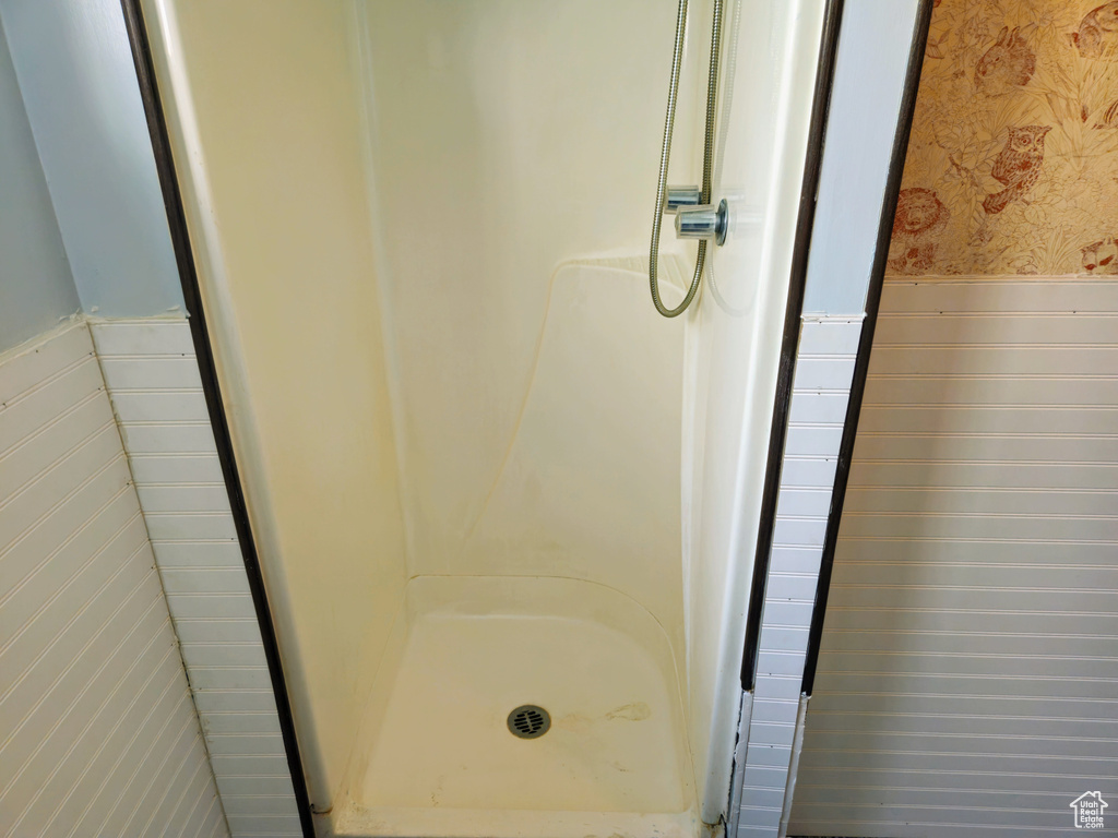Bathroom with wallpapered walls, a wainscoted wall, and a shower stall