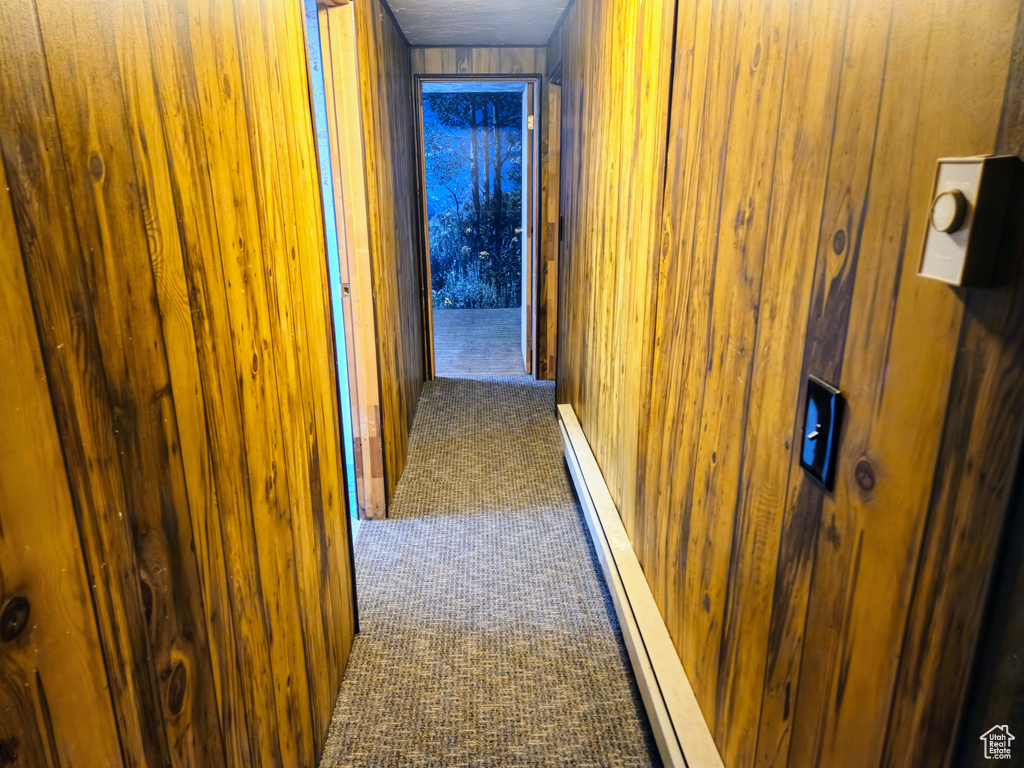 Corridor featuring dark colored carpet, wooden walls, and a baseboard radiator